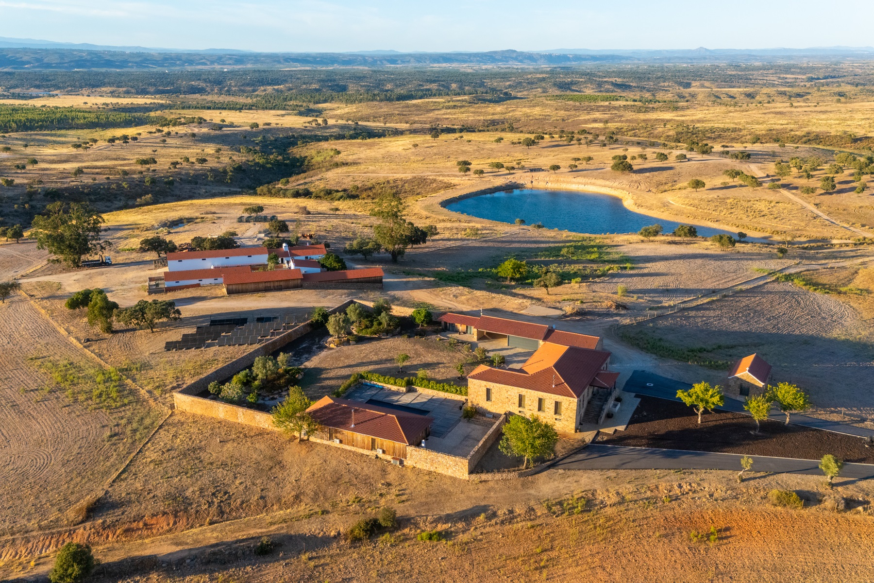 Aerial view of a rural property with stone buildings, red tile roofs, and a pond.