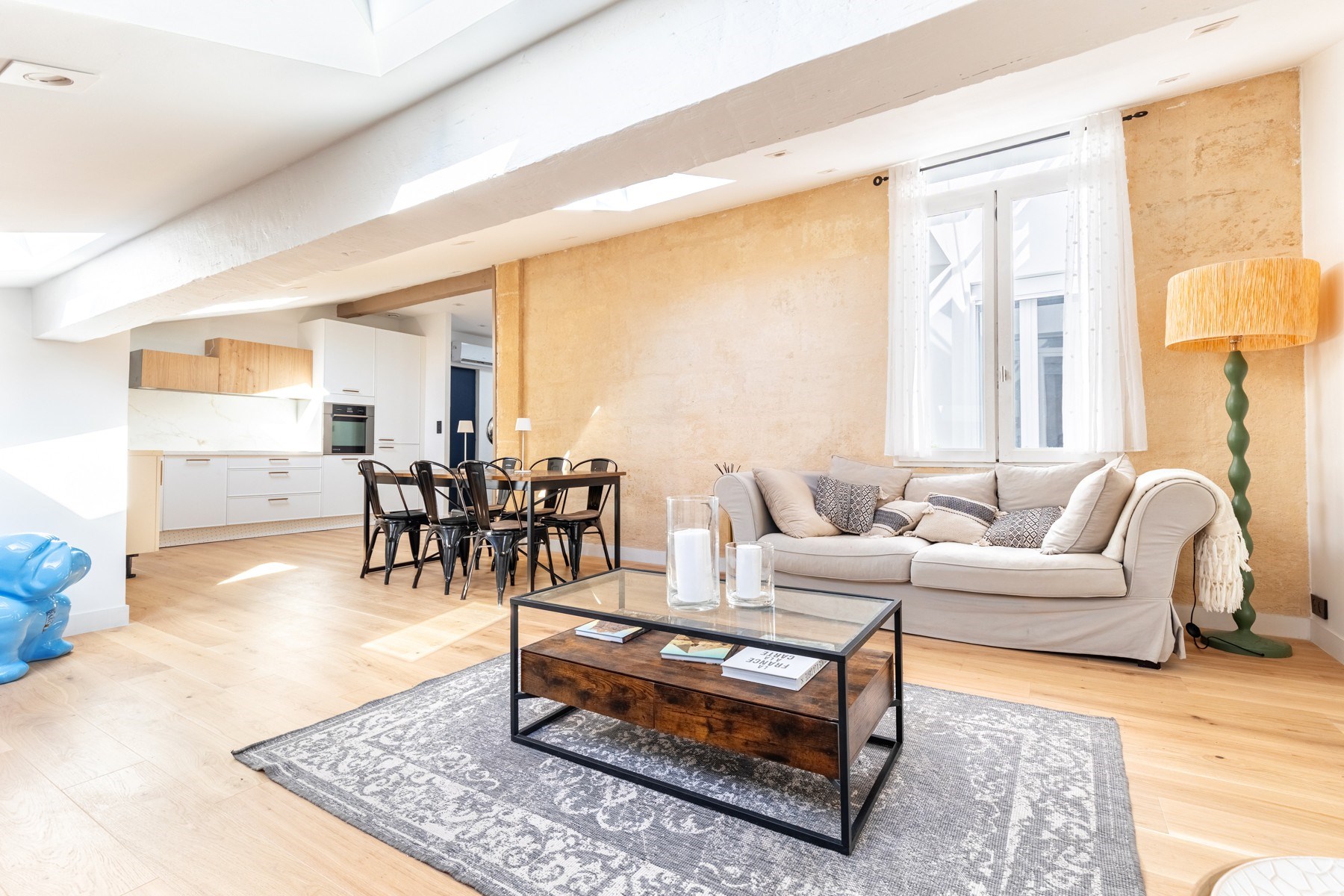 Open-plan living room and kitchen with skylights, pale wood floors, and a light sofa.