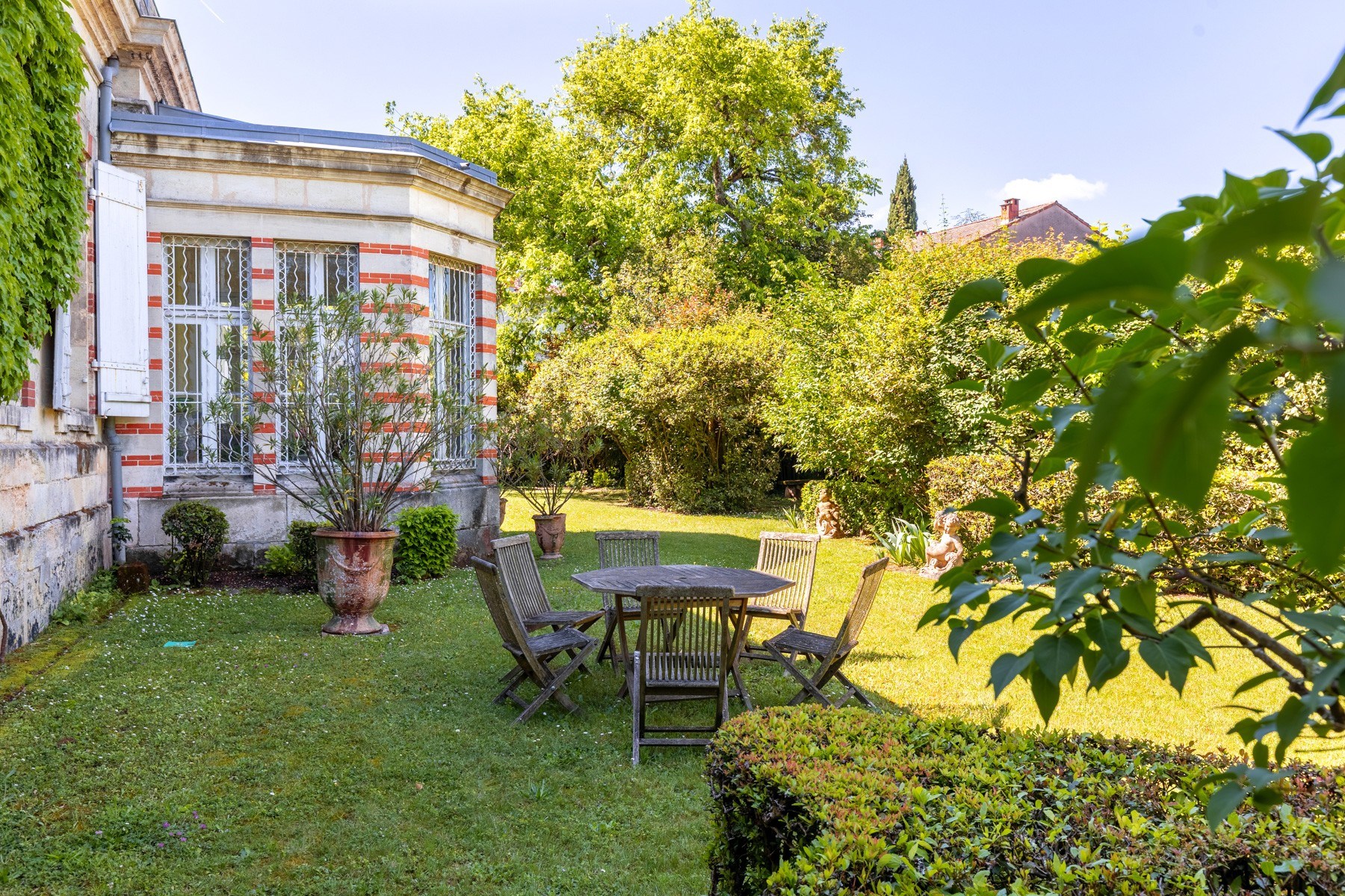 Landscaped courtyard beside a white-and-red brick house, with a wooden dining set on the lawn.