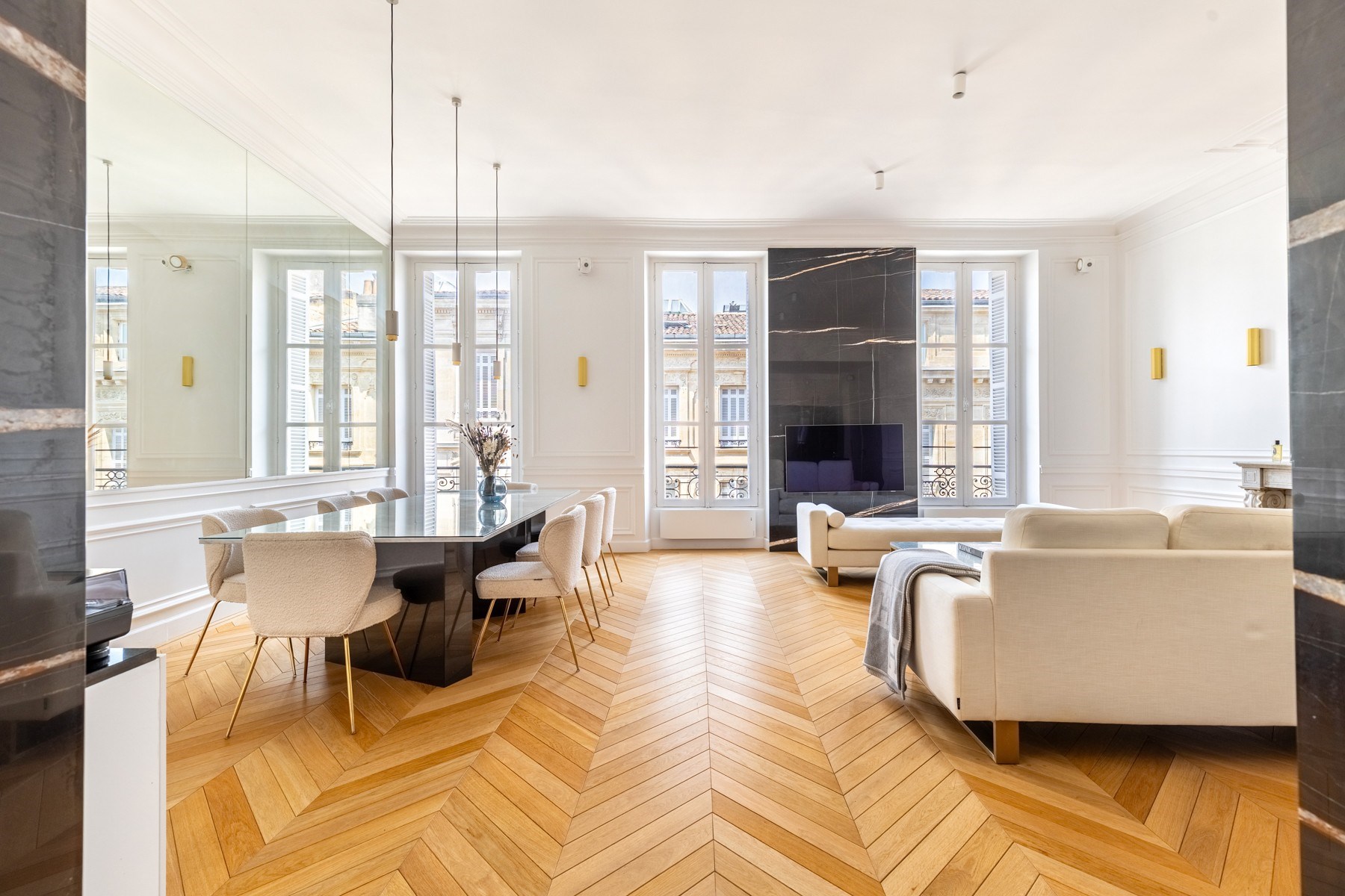 Open-plan living and dining room with a herringbone floor and dark marble television wall.