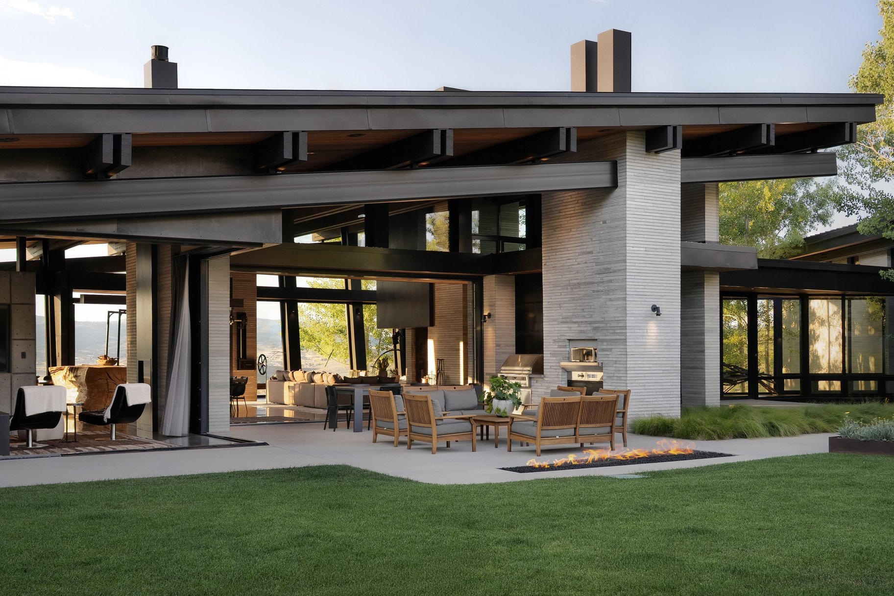 Modern Park City home with expansive glass walls, a furnished patio, linear fire pit, and mountain views.