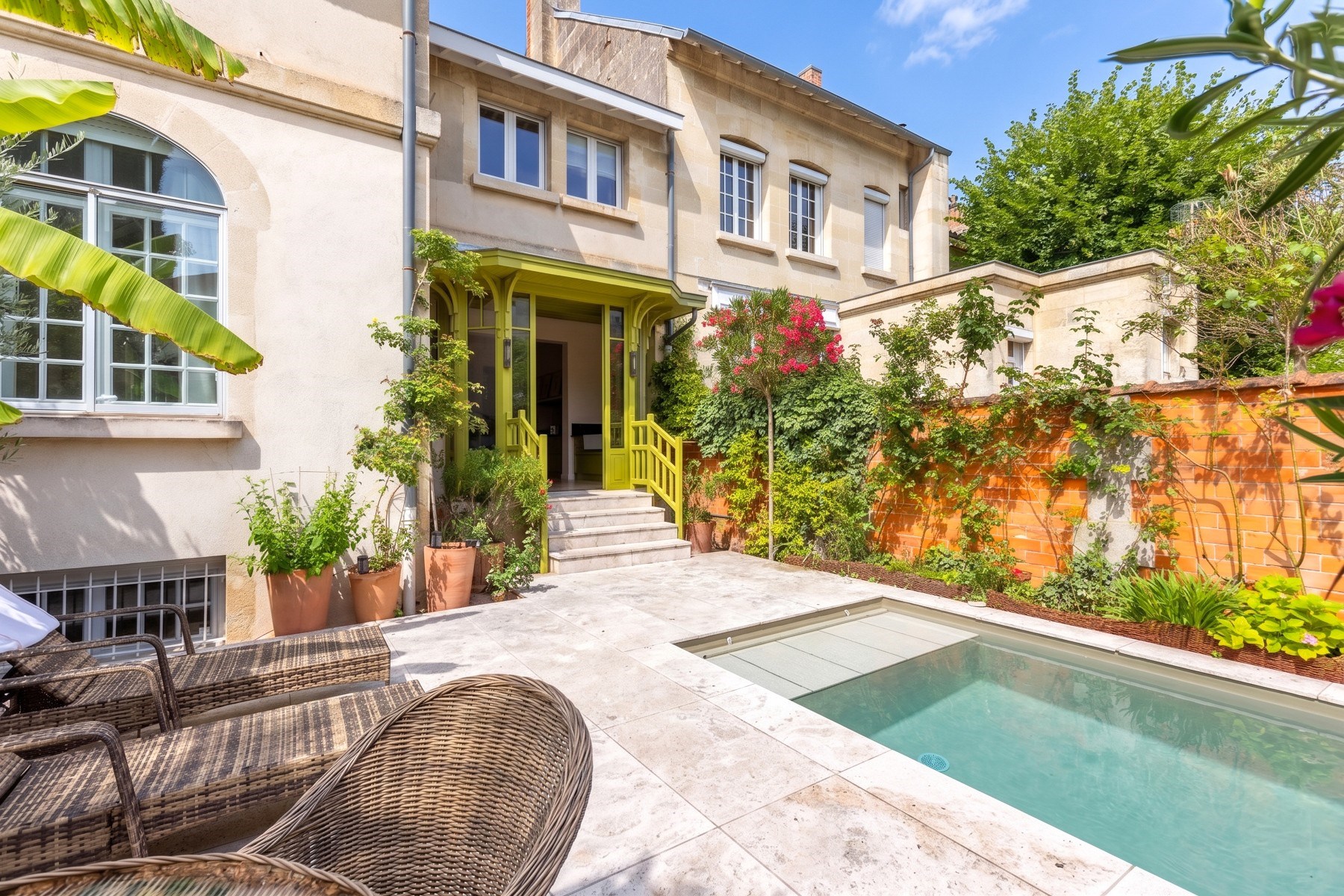 Home courtyard with a swimming pool, pale stone patio, wicker loungers, and green-trimmed entrance.