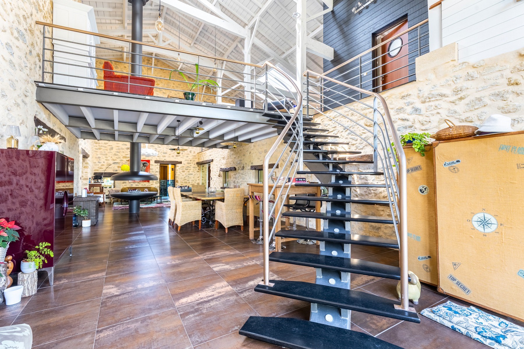 Open-plan stone interior with a dramatic dark metal staircase, mezzanine, and dining area.