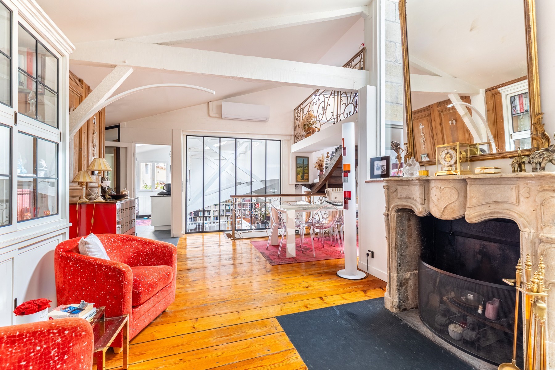 Open-plan living room with a stone fireplace, polished wood floors, and a red armchair.
