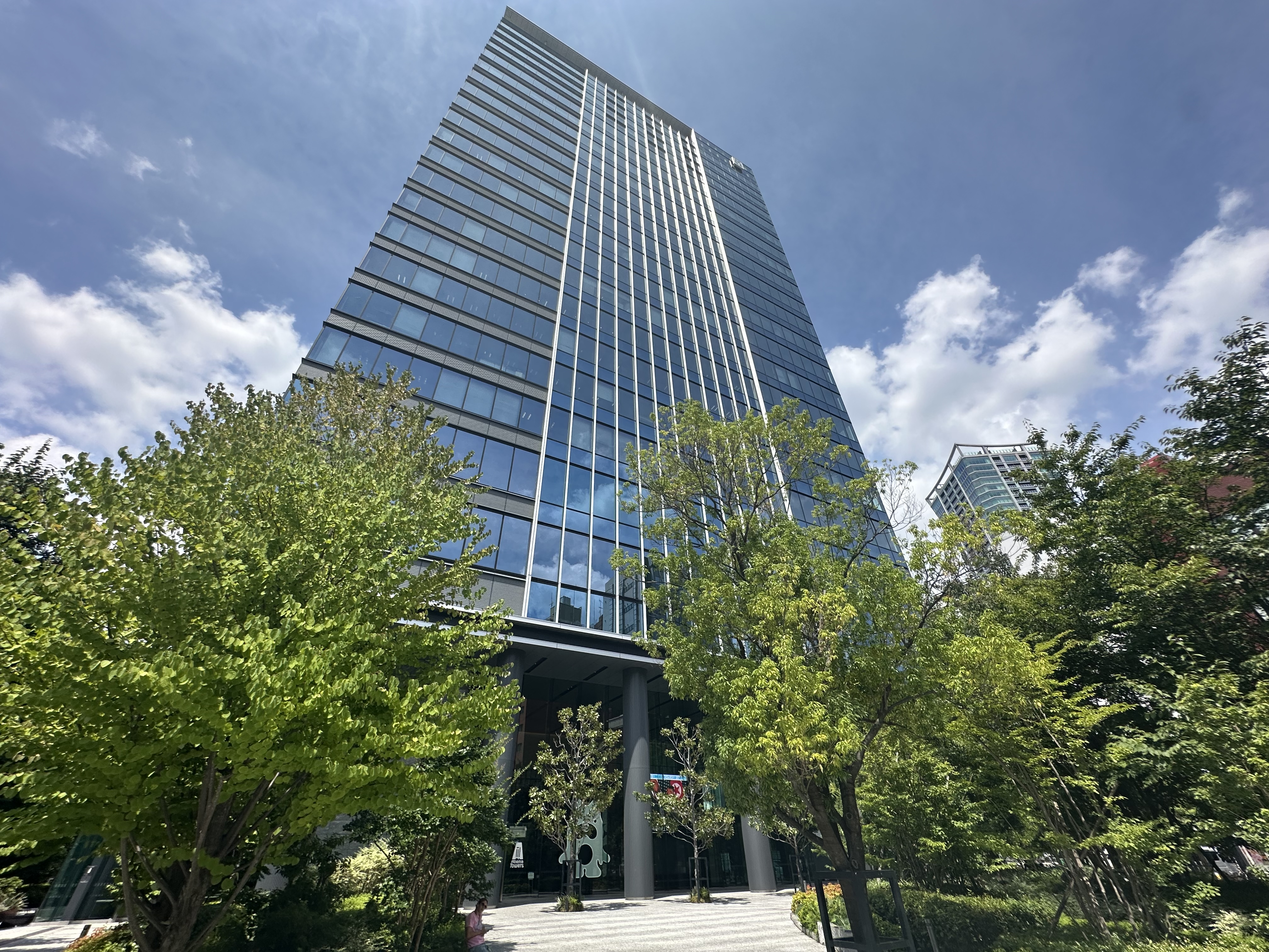 Glass high-rise with vertical white facade fins rising above leafy trees.