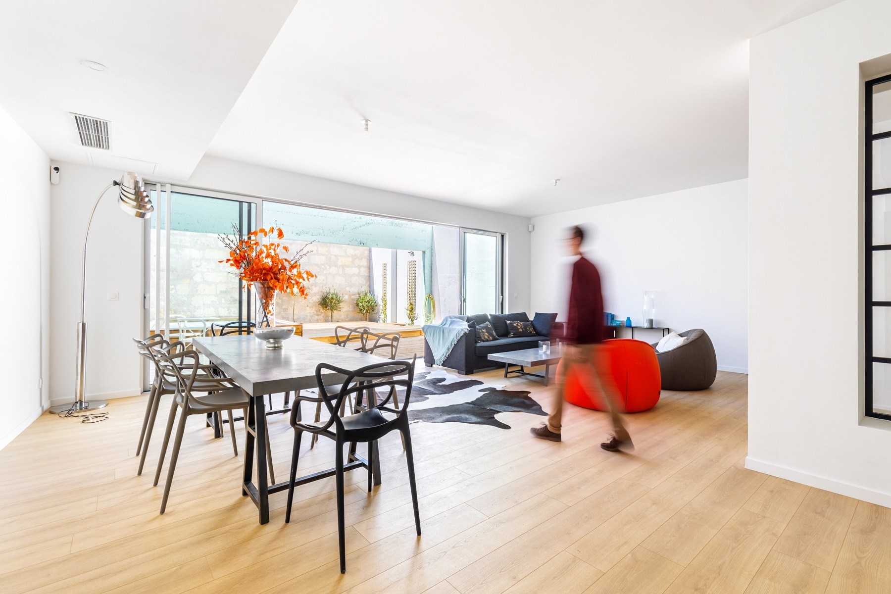 Modern open-plan living and dining room with pale wood floors and sliding doors to a patio.