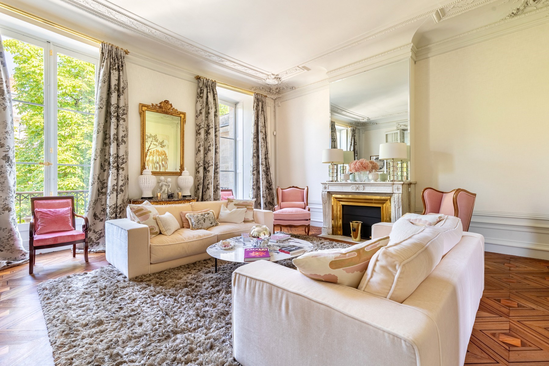 Living room with cream sofas, pink chairs, an ornate marble fireplace, and parquet floors.