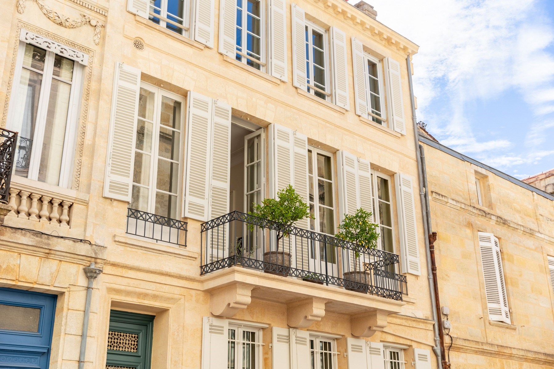 Pale stone apartment building with white shutters and iron balconies.