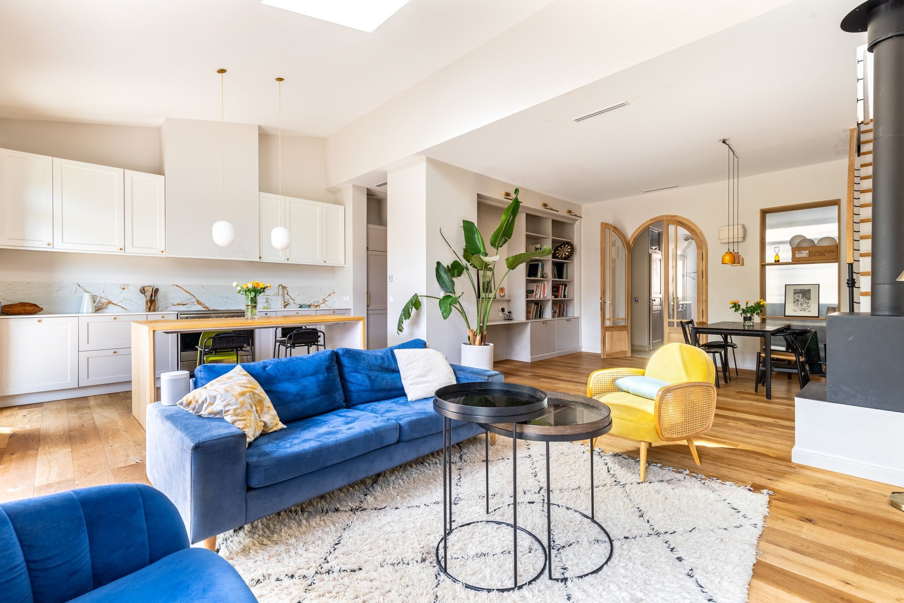 Open-plan kitchen and living room with blue sofas, a yellow chair, and warm wood floors.