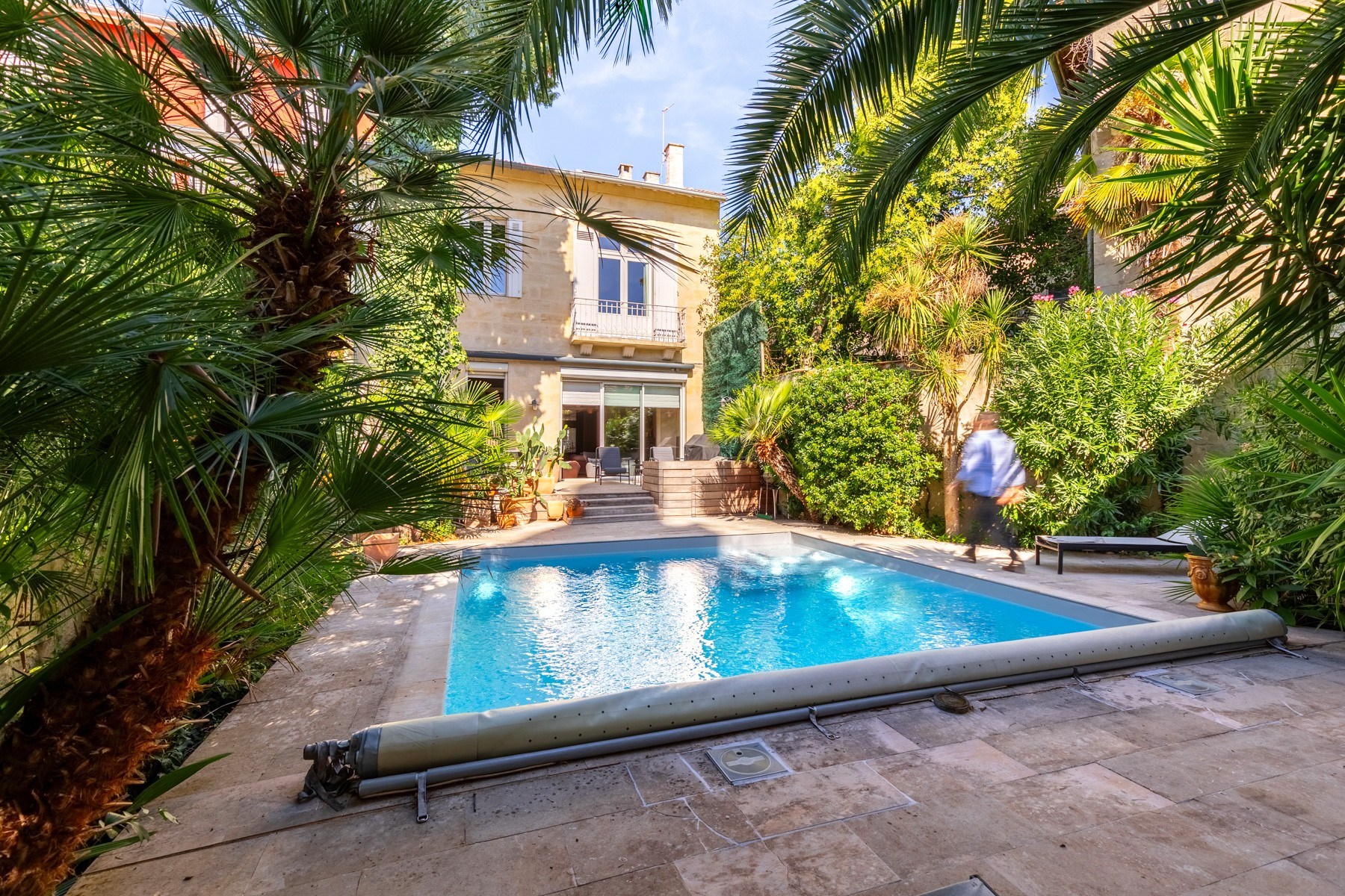 Stone house and swimming pool framed by palms and lush garden greenery.