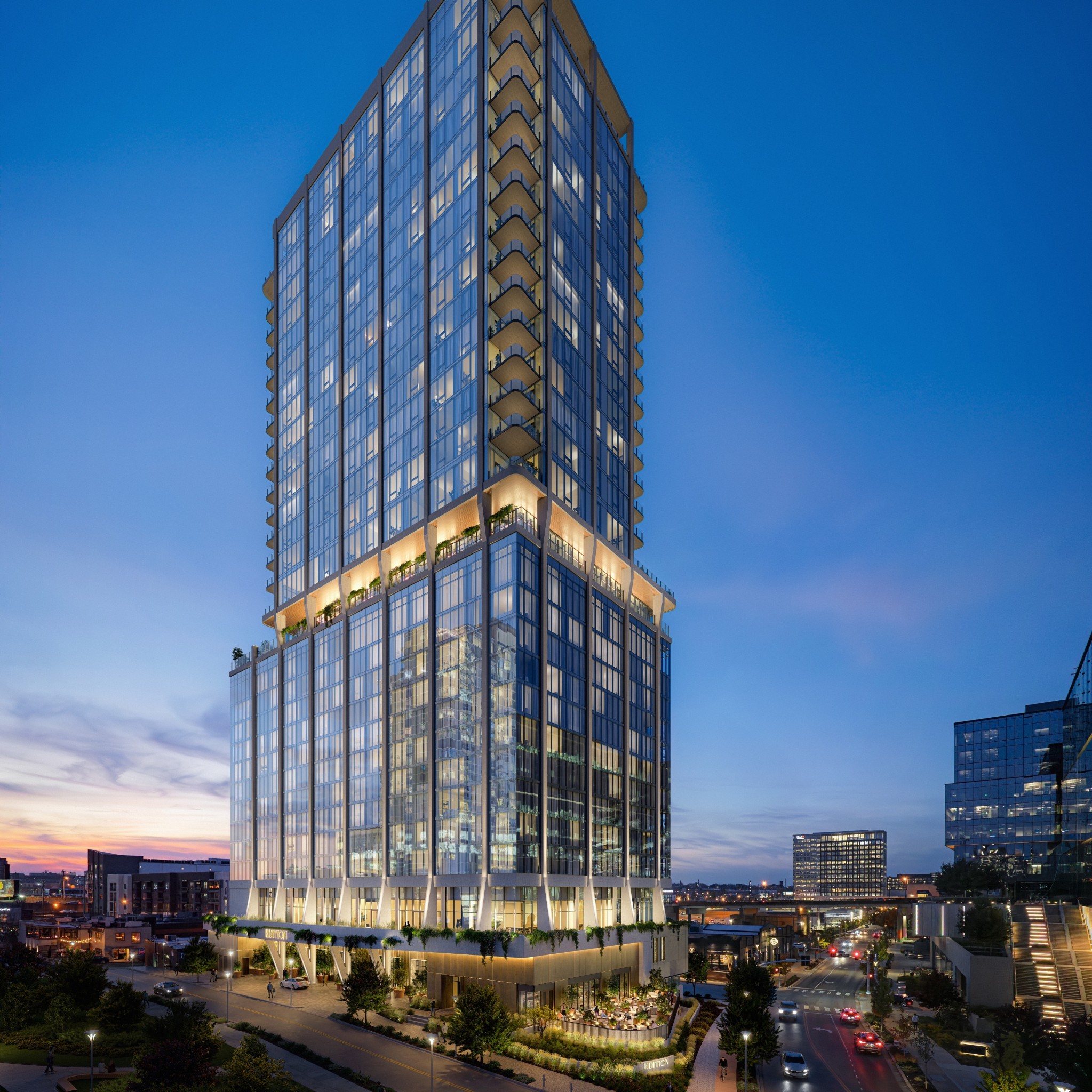 Glass high-rise with stacked balconies and illuminated terraces above city streets at dusk.