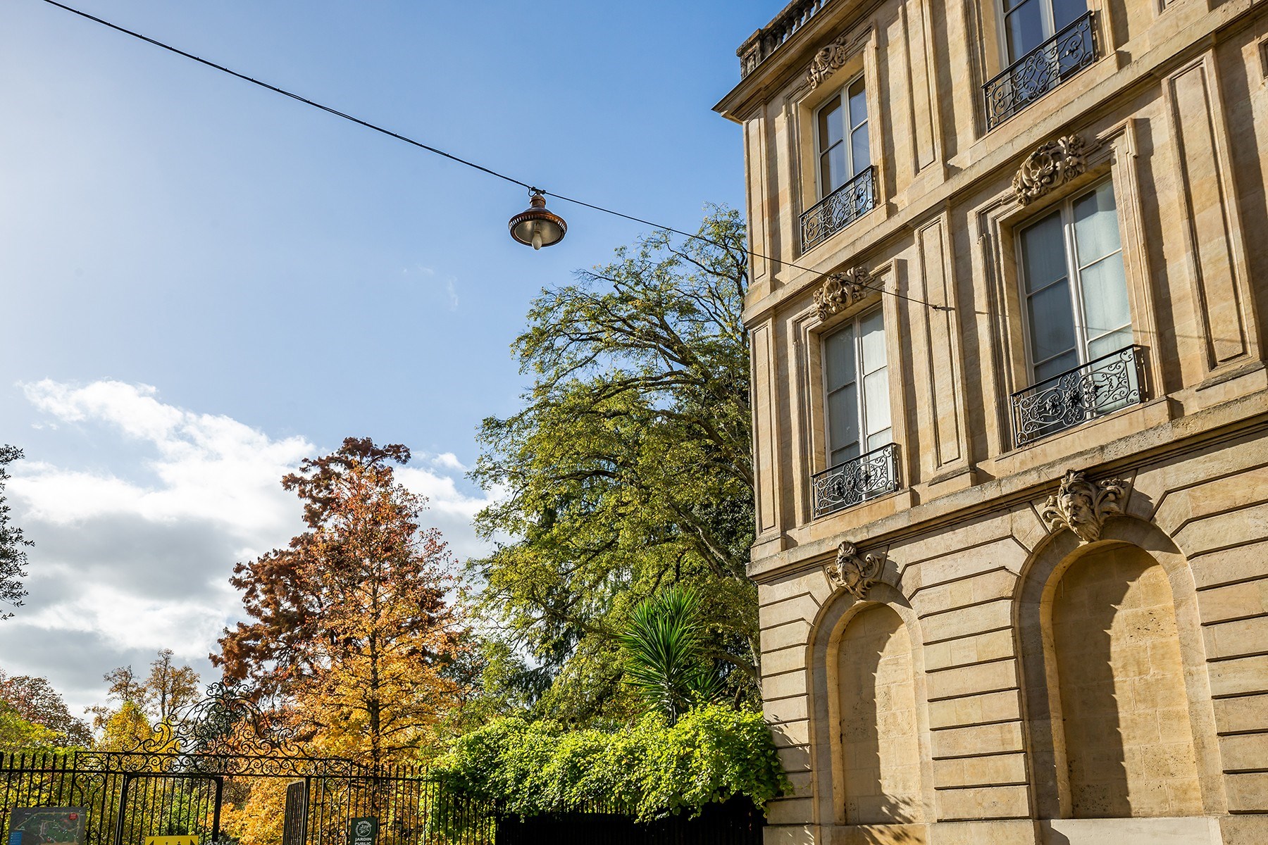 Ornate stone building beside a public garden, with wrought-iron balconies and autumn trees.
